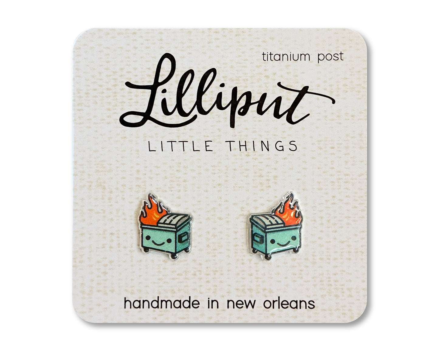 A pair of kawaii-style earrings featuring a cartoonish dumpster on fire, displayed on a card with 'Lilliput Little Things' branding.