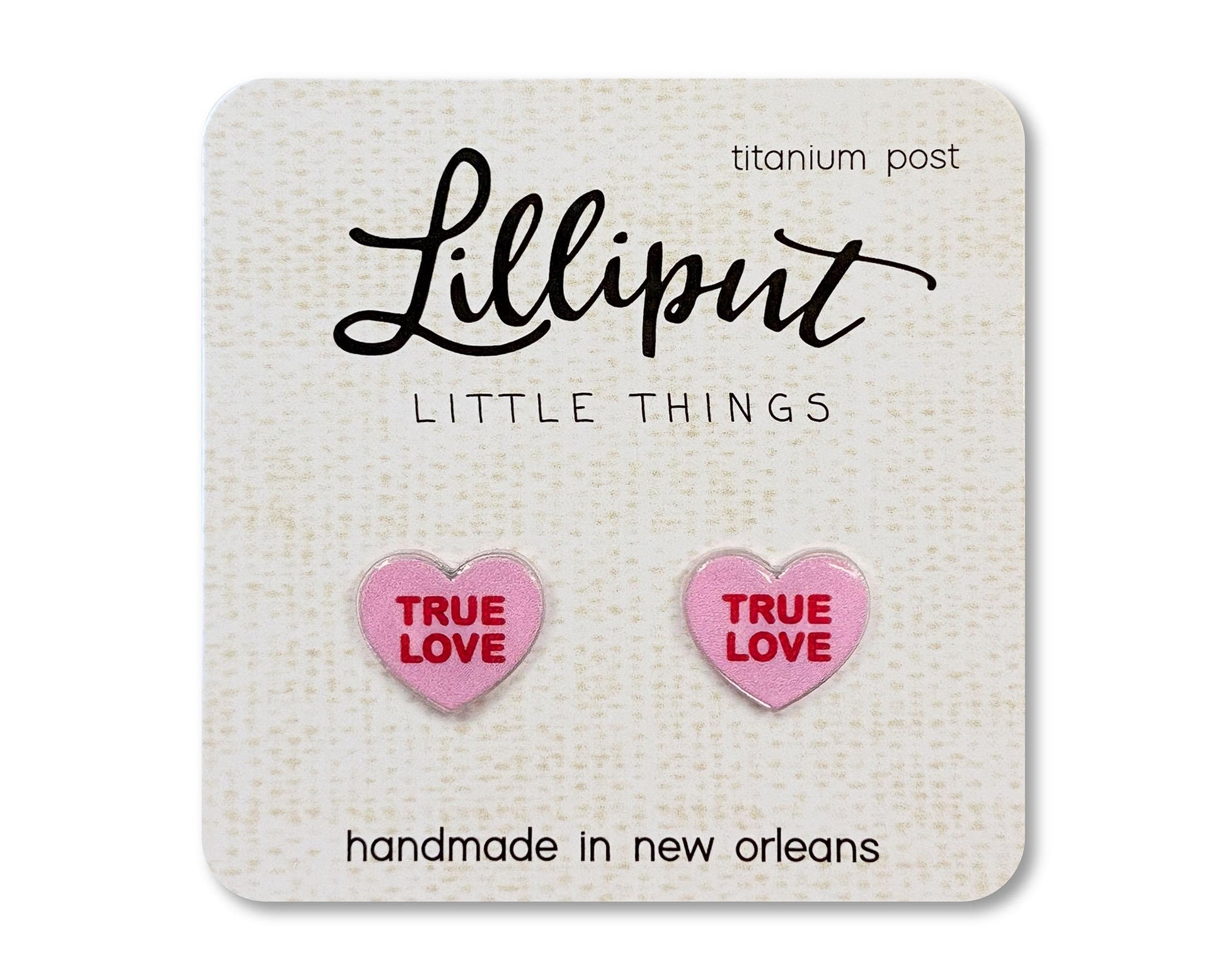 Stud earrings on a card from the brand Lilliput Little Things.  The earrings are heart shaped and pink with red text reading &quot;True Love&quot;