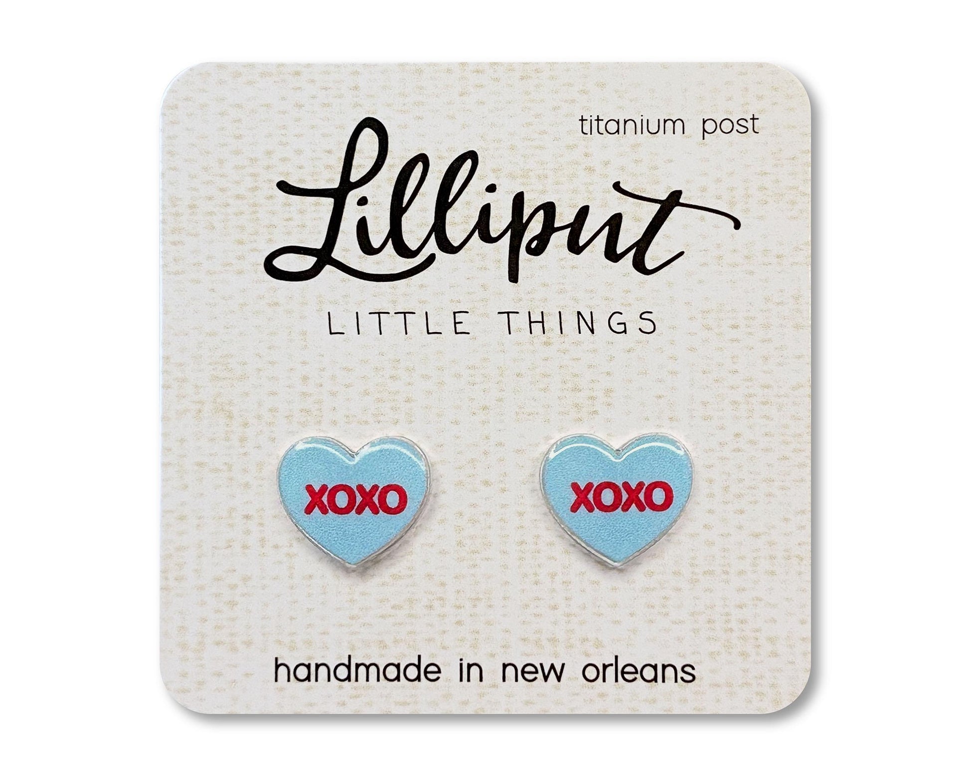 Stud earrings on a card from the brand Lilliput Little Things.  The earrings are heart shaped and blue with red text reading &quot;XOXO&quot;