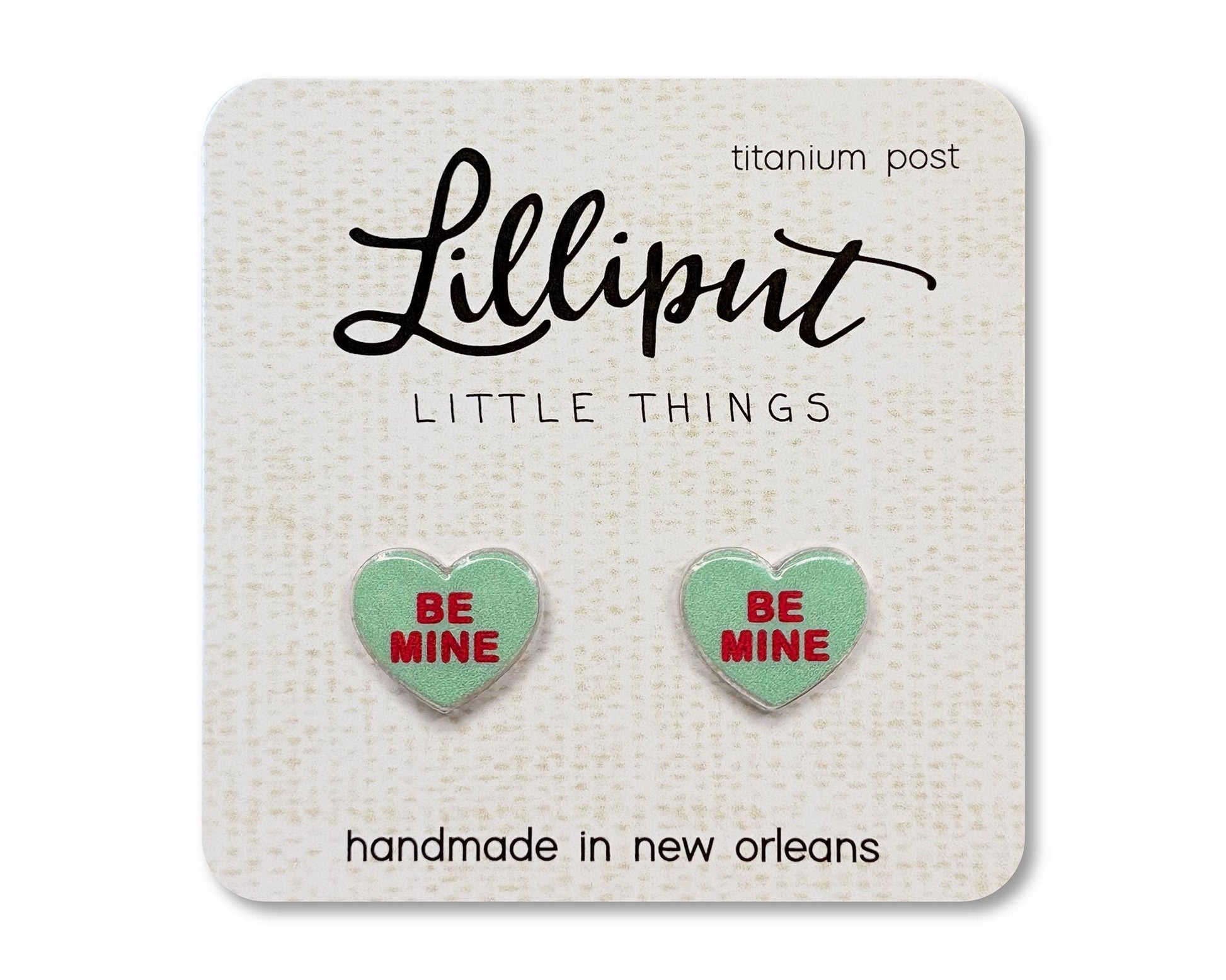 Stud earrings on a card from the brand Lilliput Little Things.  The earrings are heart shaped and green with red text reading &quot;Be Mine&quot;