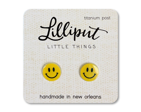 A pair of yellow happy face earrings on a branded card, labeled 'Lilliput Little Things, handmade in New Orleans, titanium post"